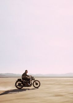 a man riding on the back of a motorcycle down a dirt road in the desert