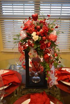 a table set with red and white plates, napkins and flowers in a vase