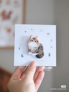 a person holding up a small card with a cat on it's back and the image of a cat is cut out