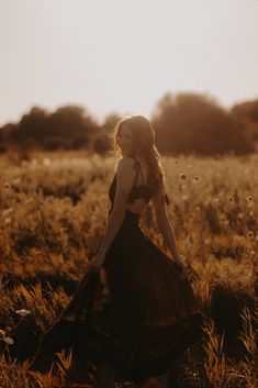 a woman standing in a field with her back to the camera, wearing a black dress