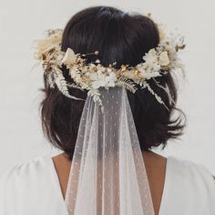 a woman wearing a veil with flowers and leaves on it's head is seen from the back