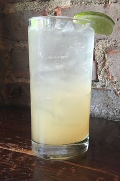 a tall glass filled with ice and lime sitting on a table next to a brick wall