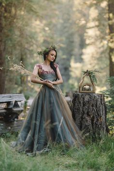 a woman standing in the woods wearing a dress with flowers on her head and wreath around her neck