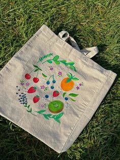 a tote bag sitting on the grass with fruit and berries painted on it's side