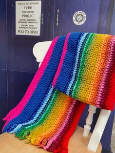 a multicolored crocheted blanket sitting on top of a white chair next to a blue door