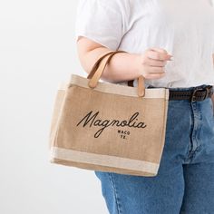 a woman is holding a bag with the name magnaslia on it and has her hands in her pockets