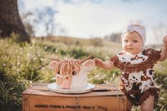 a baby girl standing next to a cow cake