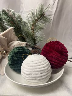 two knitted ornaments on a plate next to a pine branch and christmas tree ornament