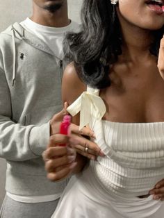 a woman in a white dress is brushing her teeth while a man stands next to her