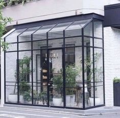 a white brick building with glass doors and plants in the windows on the side of the street