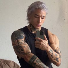 a man with white hair and tattoos on his arm is looking at his cell phone