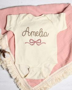 This personalized embroidered bodysuit makes a perfect baby shower, birthday, or any occasion gift for a baby!   Your baby shirt will be embroidered with the name or words of your choice (max of 10 characters), in the chainstitch script font shown in the photos. A pretty bow will be embroidered below. This item is made to order and is machine washable. See the photos for available shirt colors and size chart.  All colors of thread are available, I have too many to list!  If you would like a very Cute Personalized Cotton Onesie, Customizable Cotton Onesie For First Birthday, First Birthday Cotton Romper In Cream, Cotton Short Sleeve Onesie For First Birthday, Pink Cotton Onesie For Gift, Pink Cotton Onesie As A Gift, Pink Cotton Baptism Onesie, Pink Cotton Onesie As Gift, Personalized Cotton Onesie For Baptism