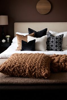 a bed with pillows and blankets on top of it in front of a brown wall