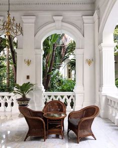 two chairs and a table in a room with white marble flooring, an archway leading to the outside