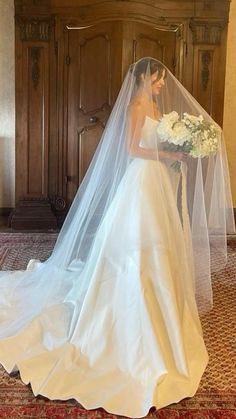 a woman in a wedding dress and veil is standing on the floor with her bouquet