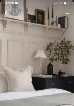 a bed with white sheets and pillows next to a shelf filled with framed pictures on the wall