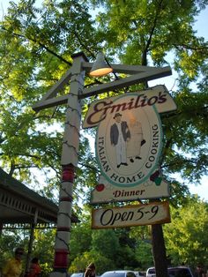 a sign for the restaurant emelios in an open - air area with cars parked nearby