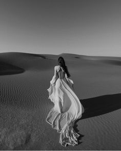 a woman in a long white dress walking through the desert