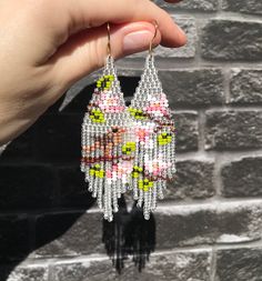 a person is holding up some beaded earrings in front of a brick wall,