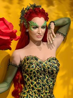 a woman with red hair and green make - up posing in front of a yellow wall