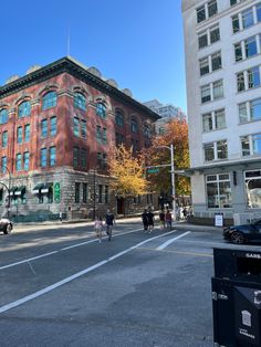 people are walking across the street in front of an old brick building on a sunny day