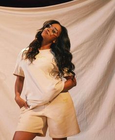 a woman standing in front of a white backdrop with her hands on her hips wearing glasses