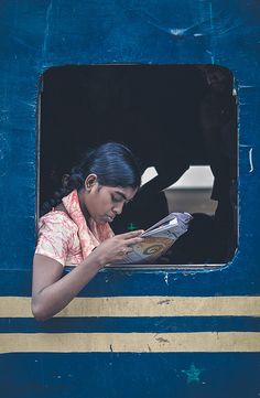 a woman reading a book while sitting in a blue and yellow train car with the window open