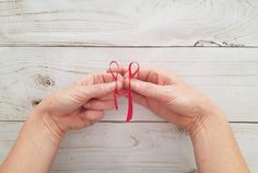 two hands holding red string on white wooden background