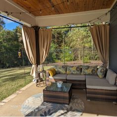 an outdoor living area with couches, tables and curtains on the side of the house