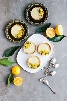 lemon tarts are served on small plates with spoons and utensils next to them