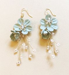 two pairs of earrings with flowers and pearls hanging from the earwires on a white surface