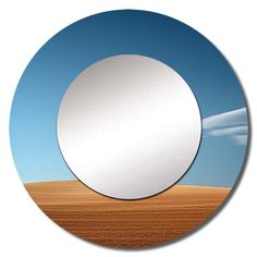 a round mirror sitting in the middle of a desert field with blue sky and clouds behind it