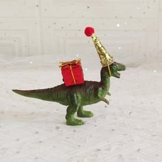 a toy dinosaur with a red gift box on its back and a gold hat on it's head