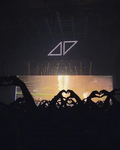 the silhouettes of people making heart shapes in front of a large screen at a concert