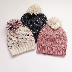 three knitted hats with pom poms on them