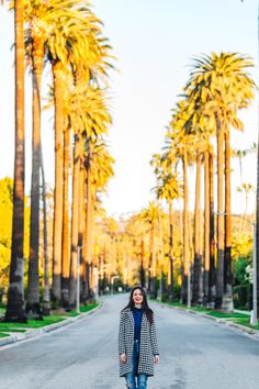 a woman standing in the middle of an empty street with palm trees on both sides