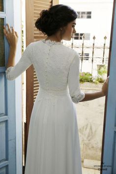 a woman standing in front of a door wearing a white dress and holding her hand out