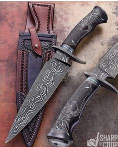 two knives with intricate designs on them sitting next to each other in leather sheaths