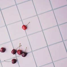 three cherries on a white tiled floor with one cherry still attached to the tile