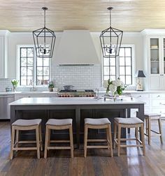 a large kitchen with white cabinets and wooden flooring, along with two dining chairs in front of the center island