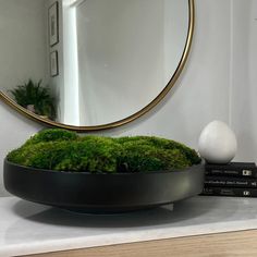 a round mirror sitting on top of a table next to a pile of green moss