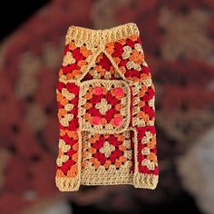 a crocheted bag hanging from a hook in the air with an orange and red pattern on it