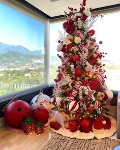 a decorated christmas tree with red and white ornaments in front of a large window overlooking the city