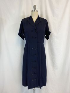 "Vintage 1950s dress featuring; ~ a v neck with notched collar short sleeves with winged cuff lightly padded shoulders collar and cuff are trimmed in velvet has two rows of buttons all the way down the front string belt loops at the waist but no belt skirt is fairly straight and falls to below the knee ~ of a mid weight faille fabric in a deep navy blue ~ labeled \"Make mine a McKettrick\" this has no size label, measurements when laid out flat are: 23 inches from pit to pit 10 inch sleeve 2 1/2 1930s Fashion Women Dresses, 1930s Fashion Women, Faille Fabric, Scrubs Dress, Bottle Blonde, Belt Skirt, Deep Navy Blue, Vintage 1950s Dresses, 1980s Dresses