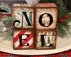 wooden blocks spelling out the word noel on top of a plate with evergreen branches and pine cones