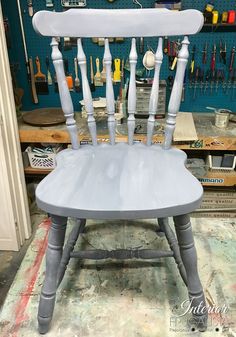 a white chair sitting on top of a wooden floor next to a wall filled with tools