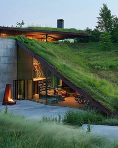 an unusual house with a green roof and grass on the top is lit up at night