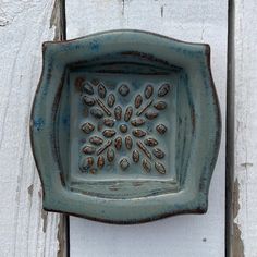 a decorative ceramic dish hanging on the side of a white wooden wall with peeling paint