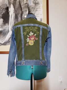 a green jean jacket with flowers on the back and blue denim sleeves, hanging from a mannequin's head