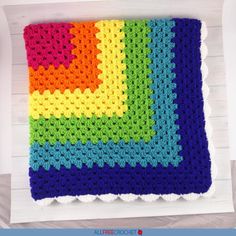 a crocheted rainbow blanket hanging on a wall with white wood planks in the background